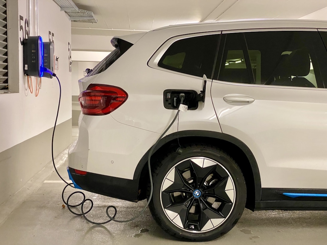 Valkoinen BMW-sähkömaasturi latauksessa modernissa autotallissa seinään asennetulla latausasemalla.