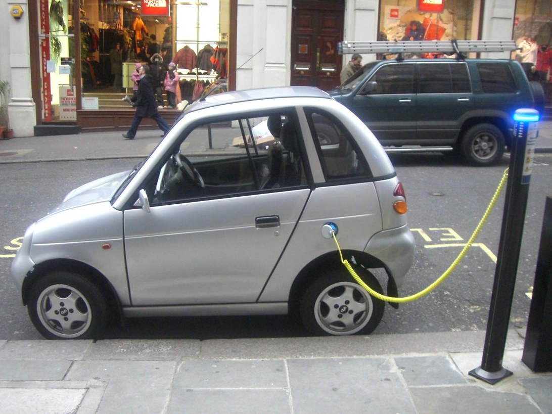 Pieni valkoinen sähköauto latauksessa kaupungin kadulla.